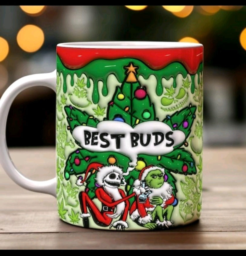 A white ceramic Christmas-themed coffee mug with a colorful graphic of the Grinch and Grizelda under a decorated tree, featuring the text 'BEST BUDS' in a speech bubble, set on a wooden surface with a blurred background.