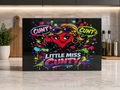 A rectangular black kitchen chopping board with a colourful cartoon graphic of a Little Miss Cunty character wearing sunglasses and speech bubbles reading 'CUNT', displayed on a marble countertop in a kitchen setting