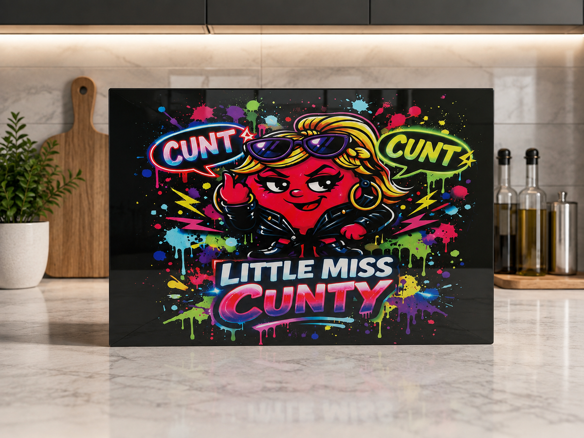 A rectangular black kitchen chopping board with a colourful cartoon graphic of a Little Miss Cunty character wearing sunglasses and speech bubbles reading 'CUNT', displayed on a marble countertop in a kitchen setting
