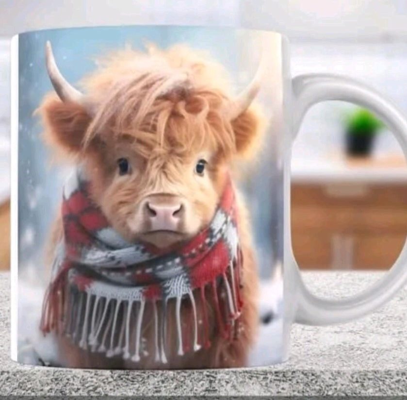 A white ceramic mug featuring a printed design of a fluffy Highland cow wearing a red, white, and gray plaid scarf, set against a snowy background.