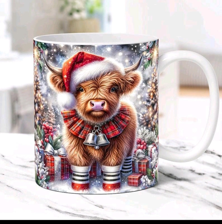 A white ceramic mug featuring a festive illustration of a fluffy brown Highland cow wearing a red Santa hat and plaid scarf, standing in a snowy holiday scene with wrapped gifts and ornaments.