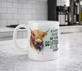 A white ceramic mug with a watercolor illustration of a Highland cow in a plaid scarf and the text 'NOBODY'S PERFECT BUT BEING SCOTTISH IS CLOSE ENOUGH!' sits on a marble kitchen countertop with a blurred kitchen background.