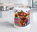 A white ceramic mug with a colourful cartoon illustration of a brown highland cow, sunflowers, butterflies, and the text 'BIT OF A Mess BUT Doin' MY BEST', sitting on a speckled kitchen countertop with a blurred kitchen background.