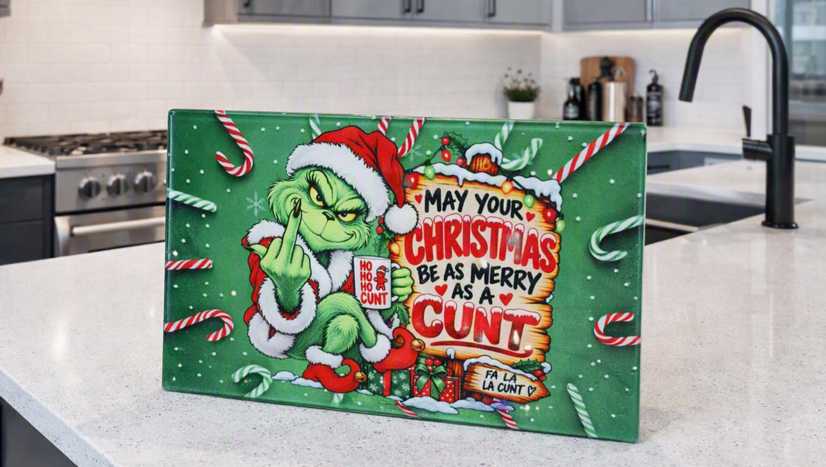 A rectangular green Christmas sign featuring the Grinch in a Santa hat with the text 'MAY YOUR CHRISTMAS BE AS MERRY AS A CUNT' and candy cane illustrations, displayed on a kitchen countertop.