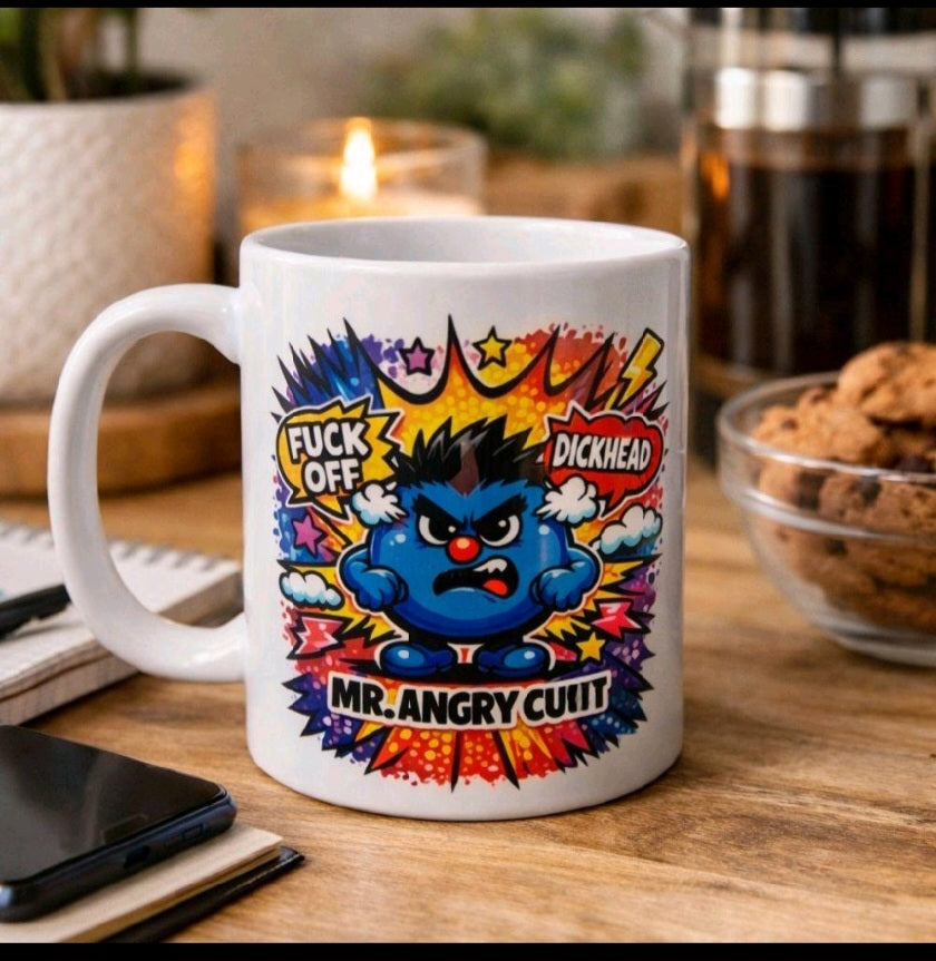 A white ceramic coffee mug with a colorful graphic of an angry blue cartoon character surrounded by comic-style bursts and text reading 'FUCK OFF', 'DICKHEAD', and 'MR. ANGRY CUNT'.