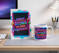 A white ceramic mug and a matching printed card stand on a desk, both featuring a colorful neon-style graphic that reads “ONLY BITCHES ARE BORN IN SEPTEMBER” over a dark background.