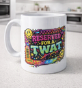 A white ceramic coffee mug with a colorful, graffiti-style graphic that reads 'RESERVED FOR A TWAT' with yellow smiley faces, set on a light gray kitchen countertop.