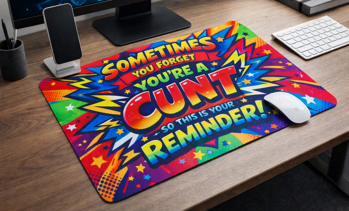 A colorful computer mouse pad with a retro comic-style design and the text 'SOMETIMES YOU FORGET YOU'RE A CUNT - SO THIS IS YOUR REMINDER!' shown on a wooden desk with a white mouse on top.