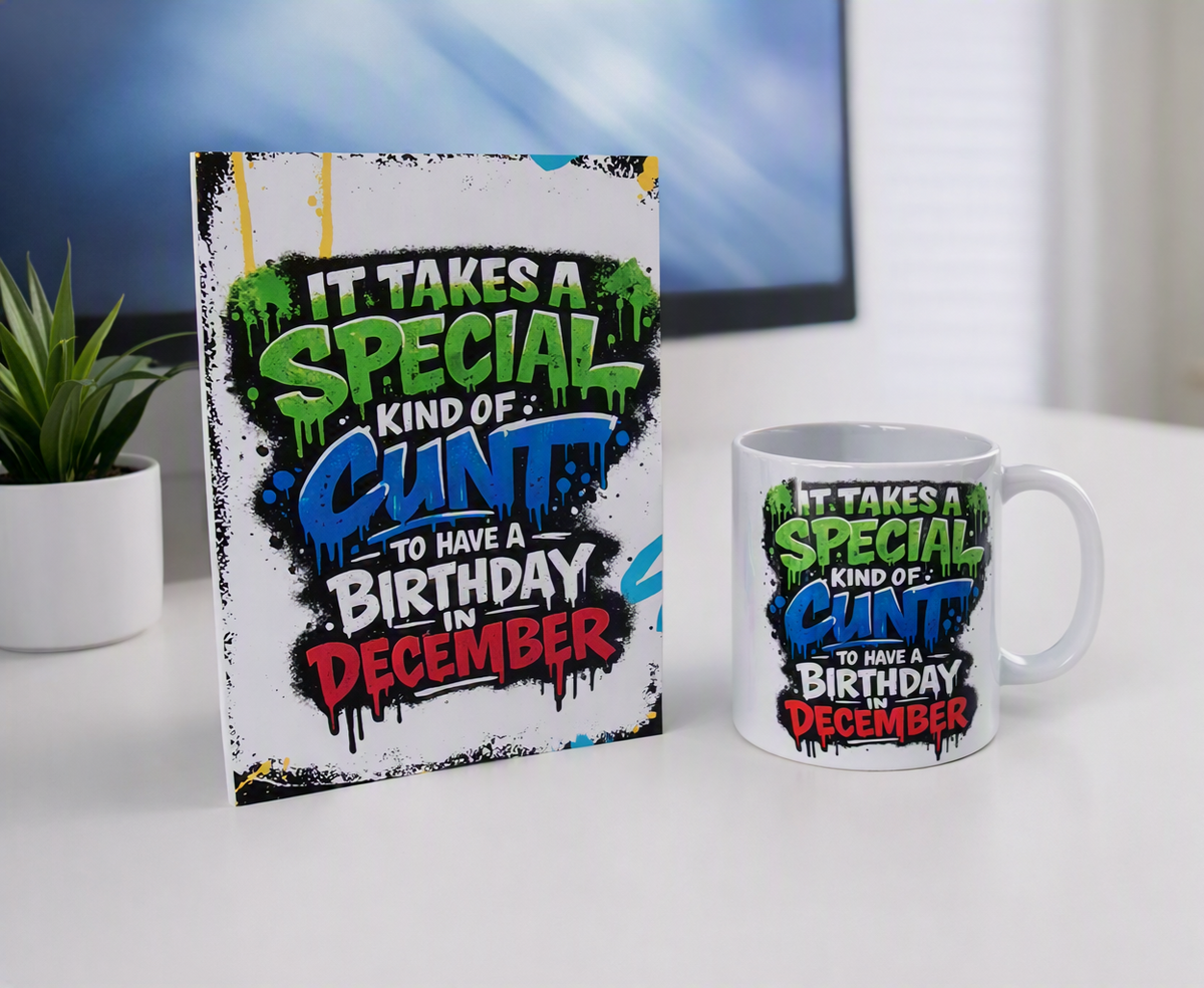 A white ceramic mug and a matching printed card standing on a white tabletop. The printed design reads, 'IT TAKES A SPECIAL KIND OF CUNT TO HAVE A BIRTHDAY IN DECEMBER' in bold green, blue, red, and black graffiti-style lettering.