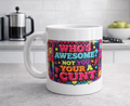 A white ceramic coffee mug with a colorful retro-style graphic that reads 'WHO'S AWESOME? NOT YOU YOUR A CUNT' in pink, yellow, and blue lettering, set on a kitchen countertop with a blurred background.