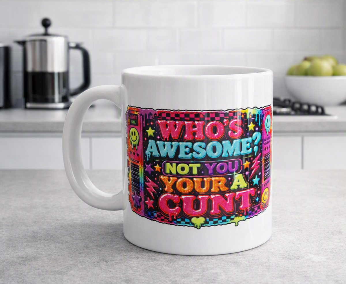 A white ceramic coffee mug with a colorful retro-style graphic that reads 'WHO'S AWESOME? NOT YOU YOUR A CUNT' in pink, yellow, and blue lettering, set on a kitchen countertop with a blurred background.